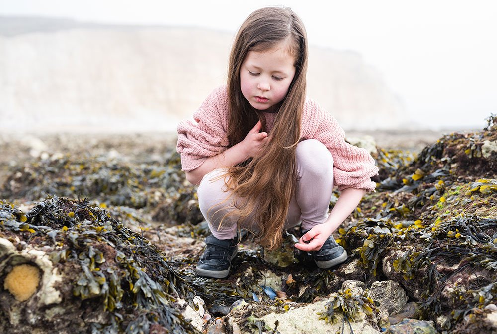 girl playing with seaweed on a pebble beach