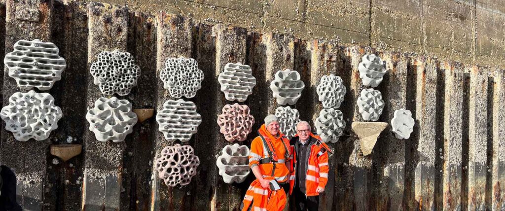 Two staff members from Newhaven Port standing in from of a living sea wall at Shoreham