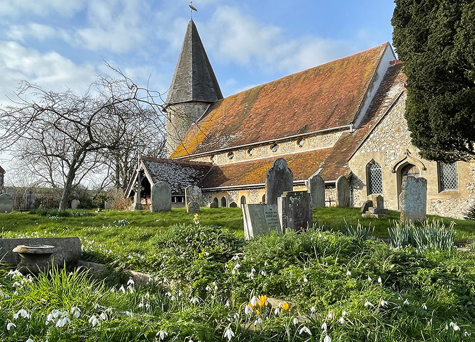 Norman Church at Piddinghoe from the churchyard with snowdrops and headstones