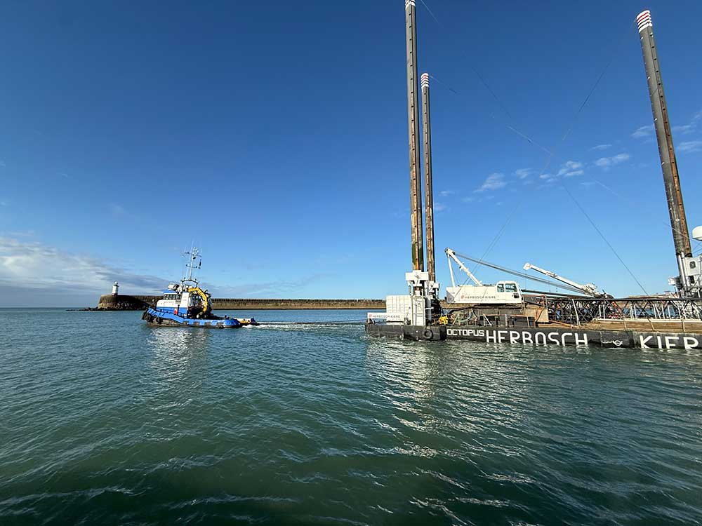 A blue tug tows the Octopus platform past the Newhaven lighthouse