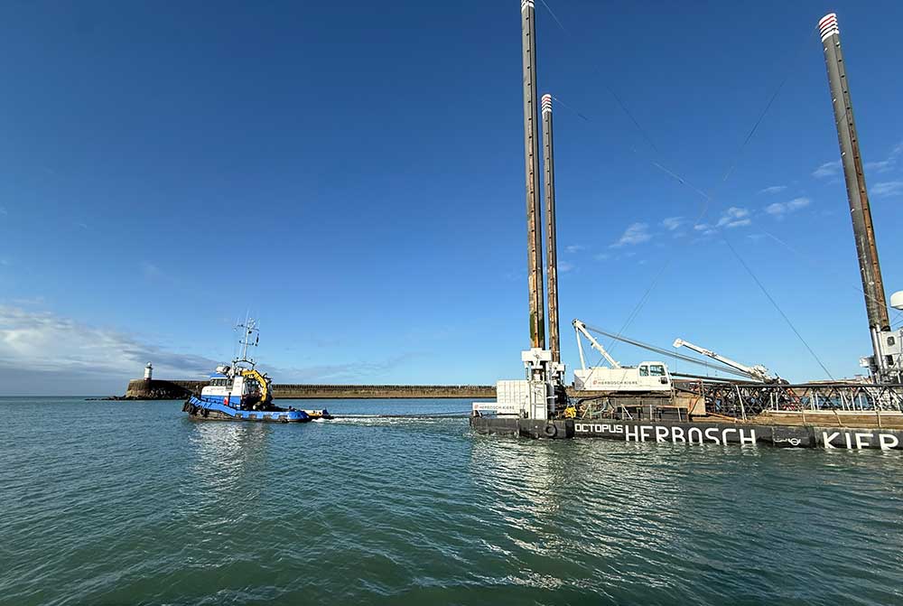 The Herbosch Kiere platform passes Newhaven Port lighthouse being towed by a blue tug